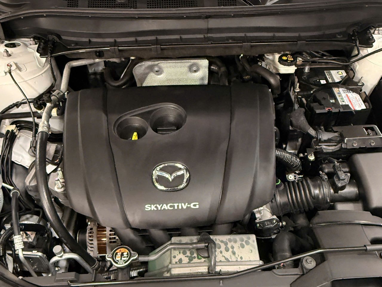 Khoang máy Mazda CX-5 sau khi vệ sinh tại QC Auto, nắp che động cơ đen đều màu, sạch bụi dầu