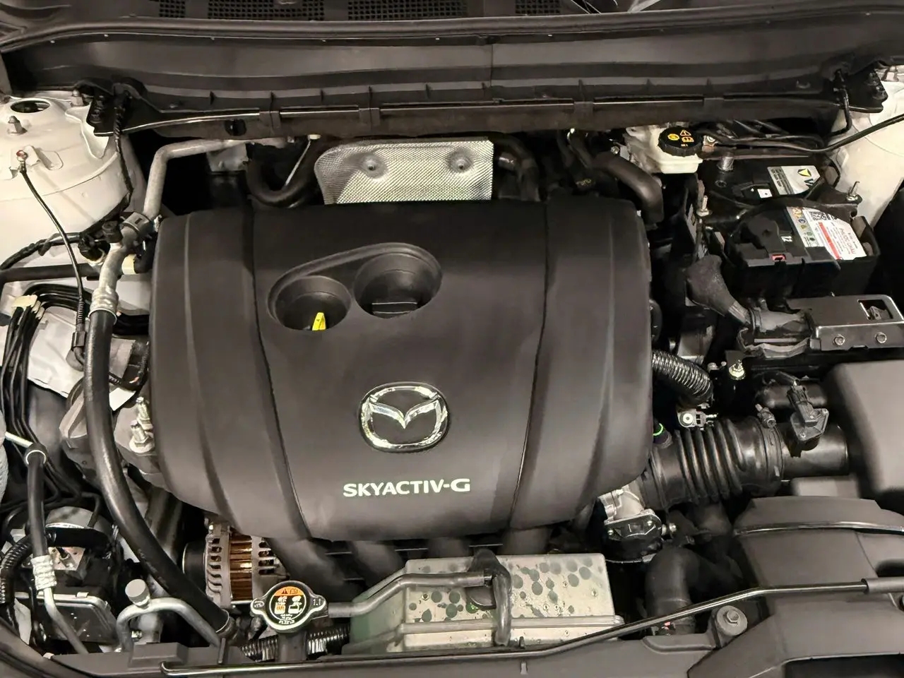 Khoang máy Mazda CX-5 sau khi vệ sinh tại QC Auto, nắp che động cơ đen đều màu, sạch bụi dầu